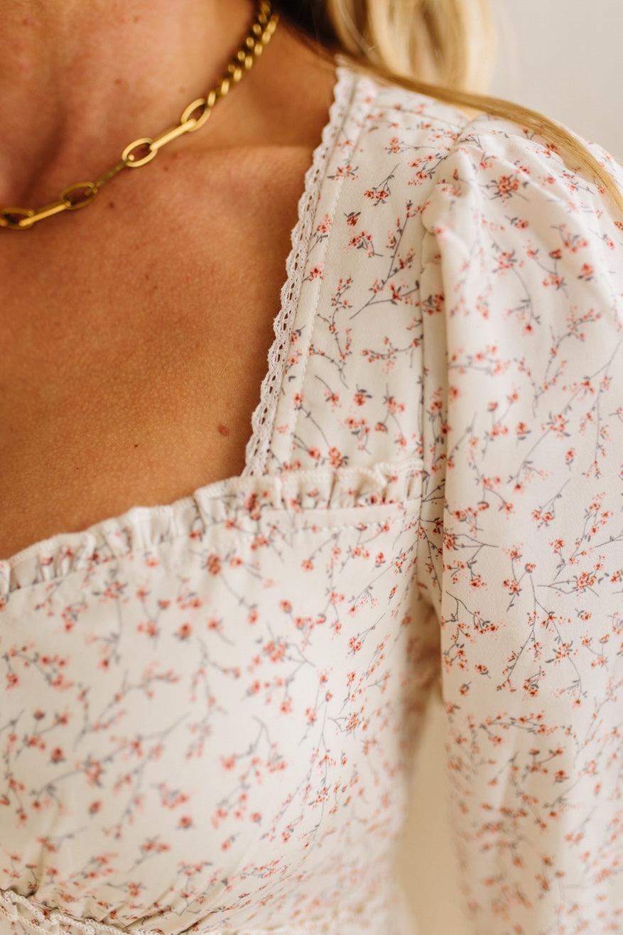 Close-up of a person wearing a white floral dress with a gold chain necklace.