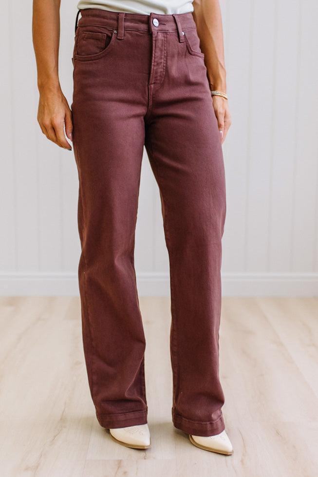 Woman wearing dark brown high rise pants with wide leg cut, on a light wood floor with neutral background.