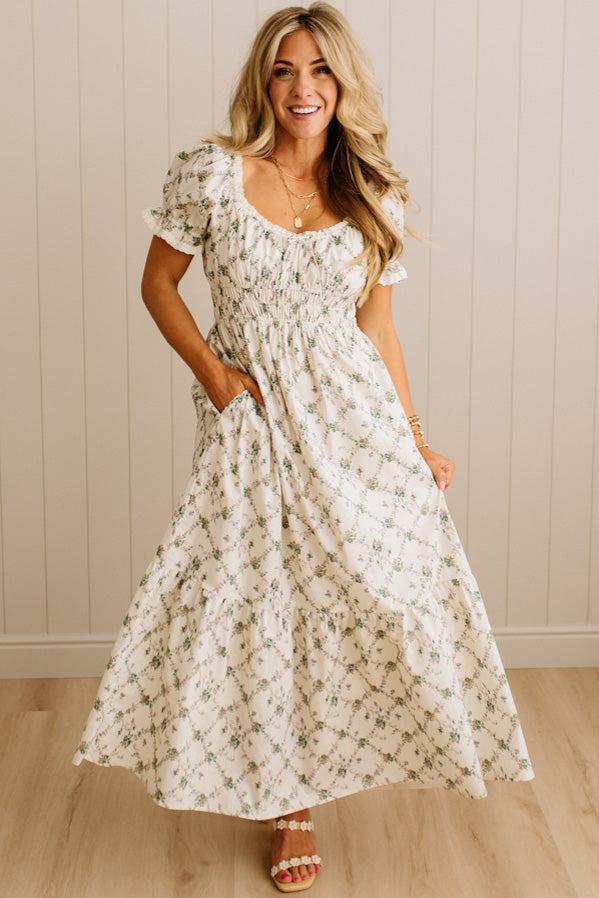 Woman wearing a floral dress standing against a neutral wall.
