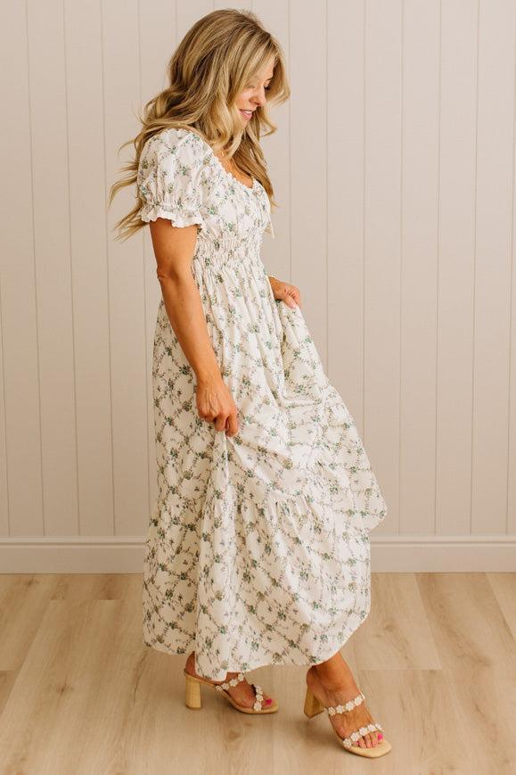 Woman wearing a floral dress standing against a beige wall.