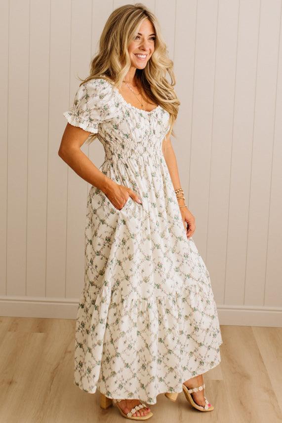 Woman wearing a floral dress standing against a wooden paneled wall.
