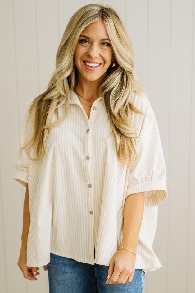 Woman wearing a white button-up shirt and blue jeans against a light wooden panel background