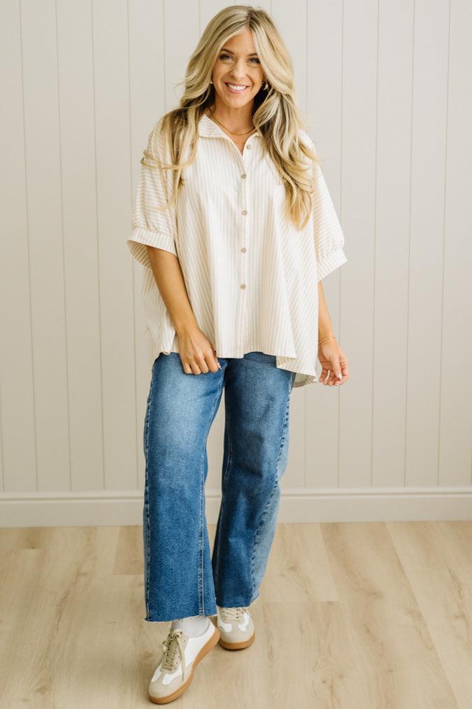 Woman wearing a white blouse and blue jeans standing in a room with a light wooden floor and white paneled wall.