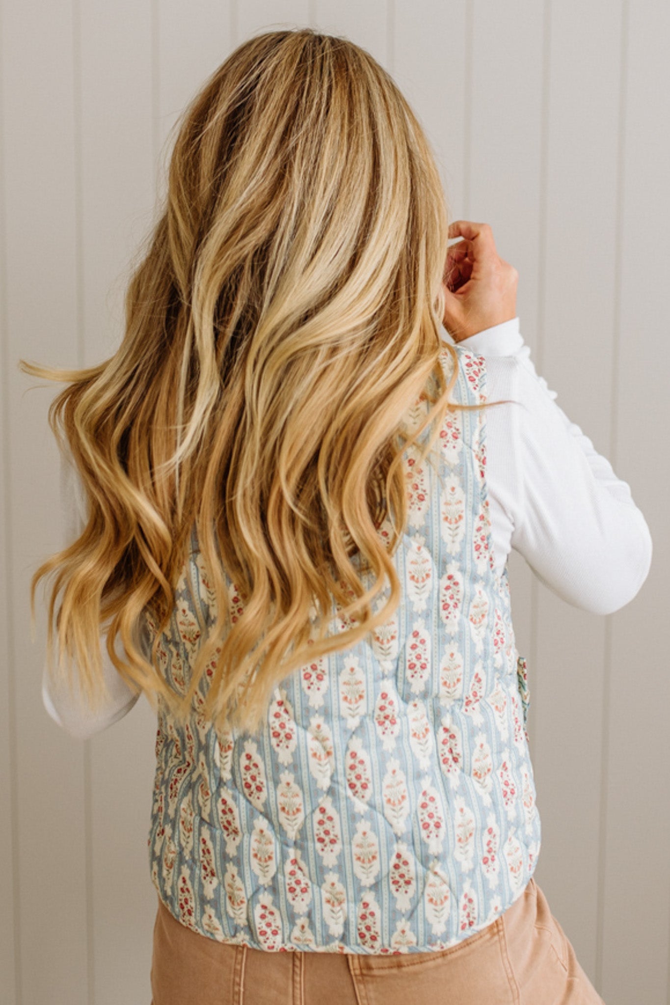 Person wearing a floral patterned vest over a white shirt with a neutral background