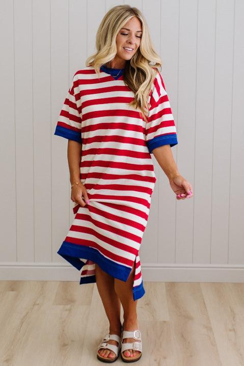 Woman wearing a red and white striped dress with blue trim against a white paneled wall.