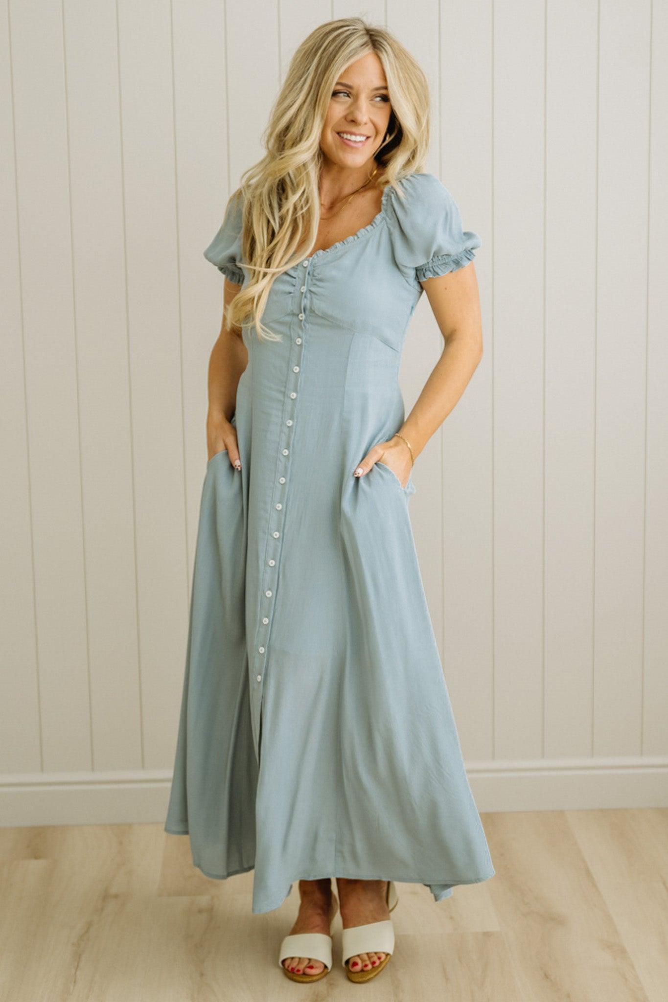 Woman wearing a light blue dress standing against a white paneled wall.