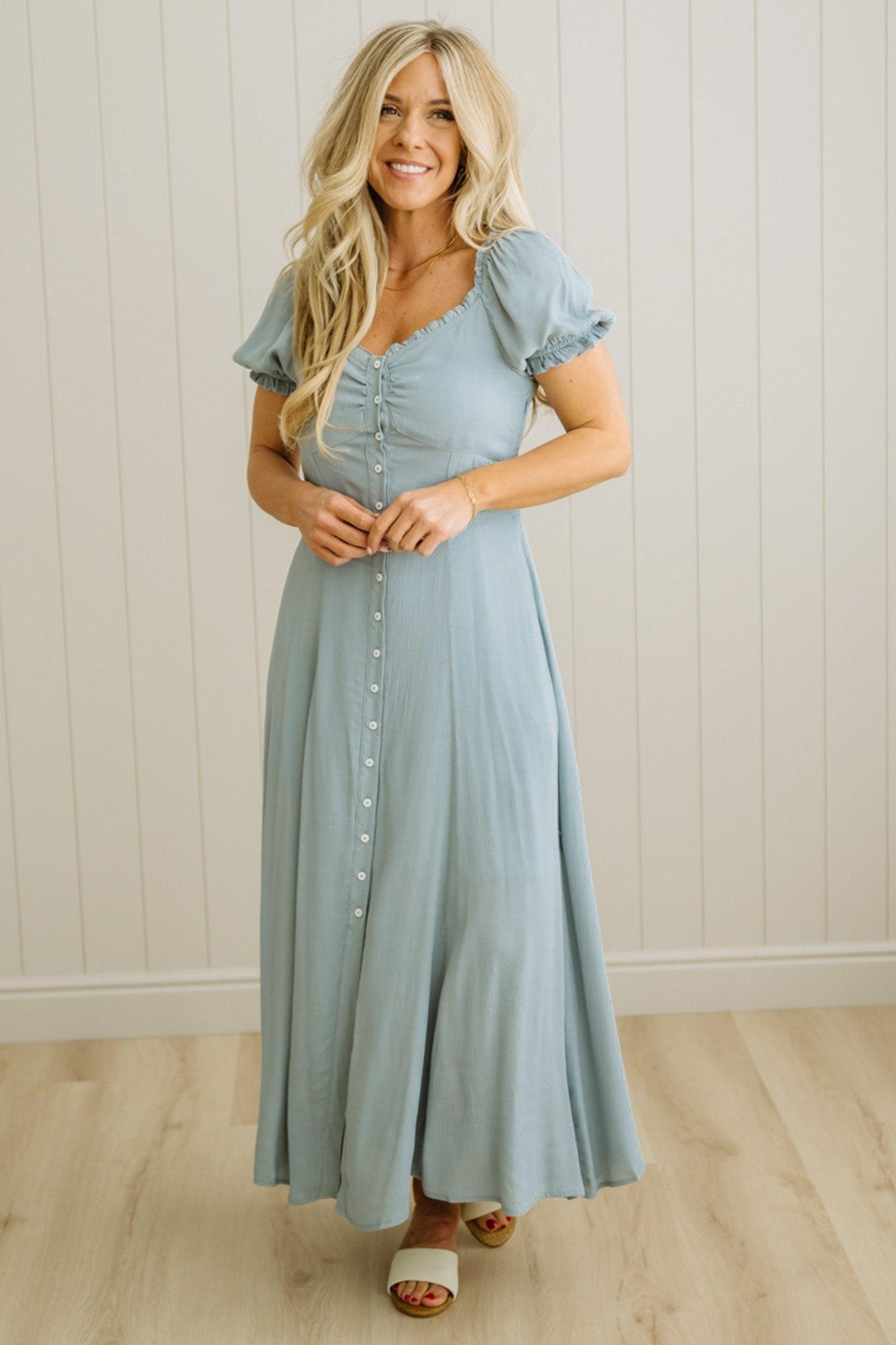 Woman wearing a light blue dress standing against a white paneled wall.
