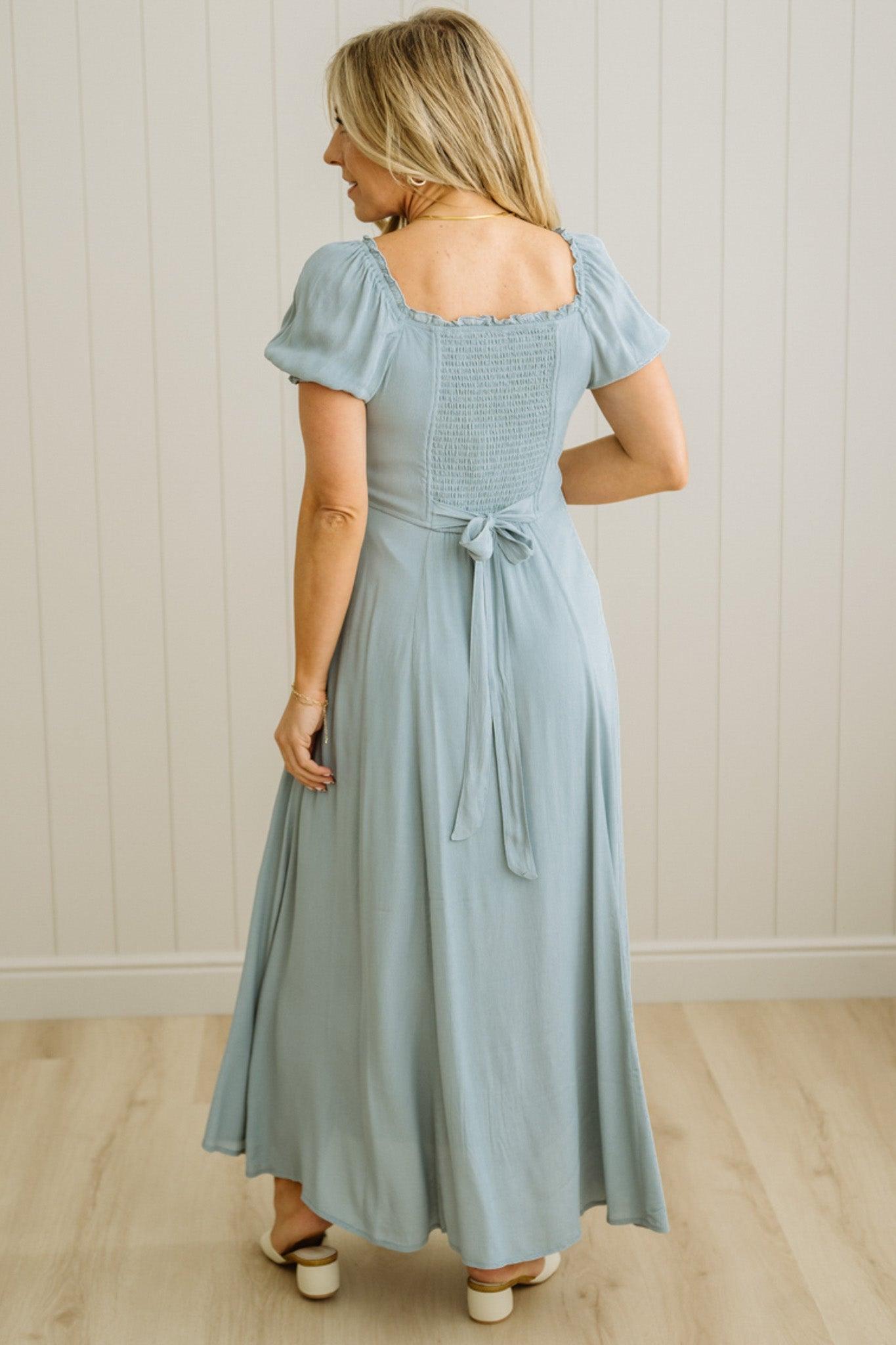 Woman wearing a light blue dress with a belt in a minimal indoor setting