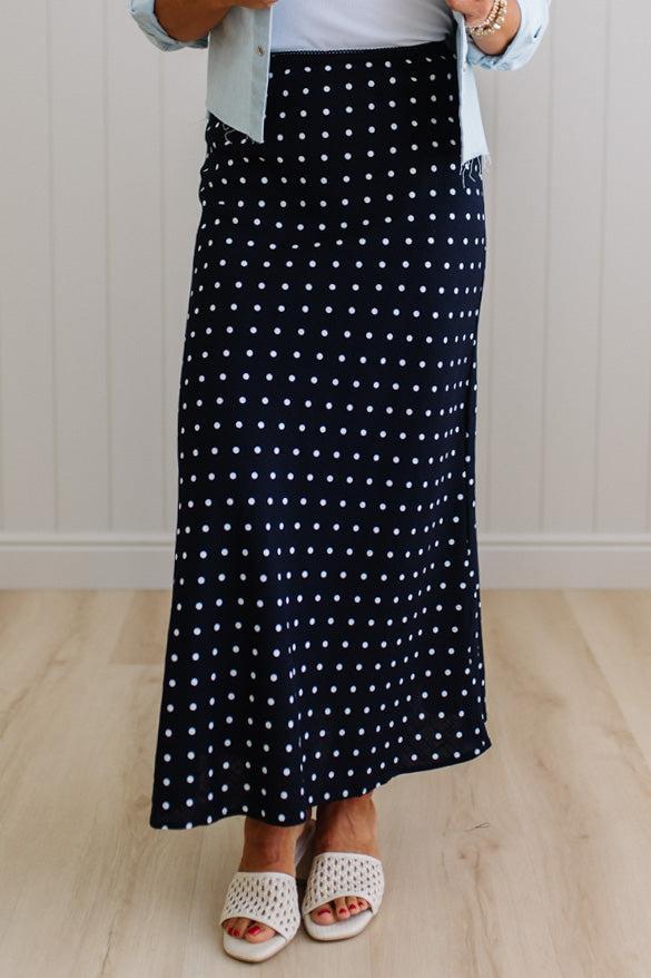 Person wearing a black polka dot skirt on a wooden floor.