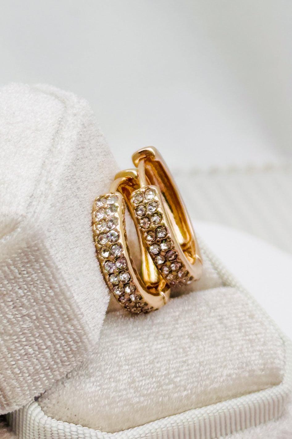 Gold hoop earrings with embedded stones on a white fabric background
