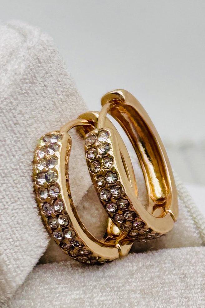 Gold hoop earrings with embedded crystals on a soft fabric background