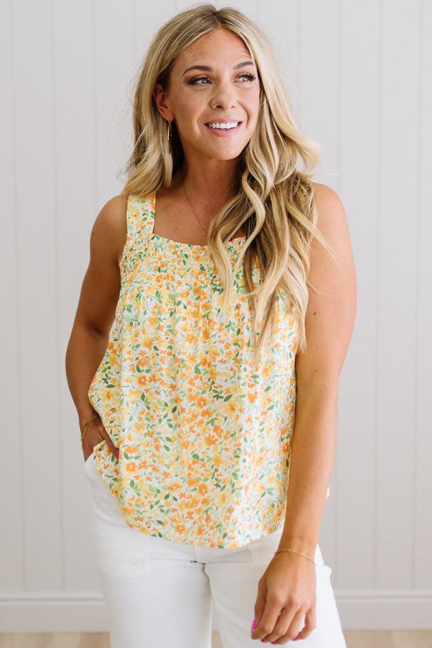 Woman wearing a floral sleeveless top and white pants against a light background