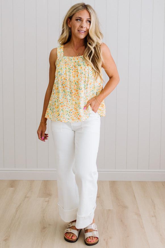 Woman wearing a floral top and white pants standing against a light wooden panel background
