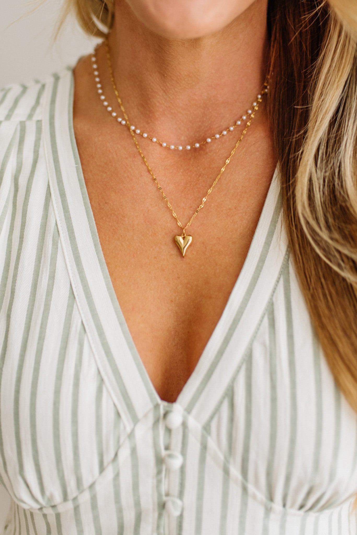 Close-up of a person wearing a gold heart-shaped necklace with a blurred background