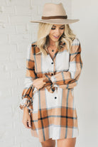 Blonde woman in a fedora wearing a large plaid printed knee length dress with collar, button front, long sleeves with ruffled wrist.
