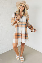 Blonde woman in a fedora wearing a large plaid printed knee length dress with collar, button front, long sleeves with ruffled wrist.