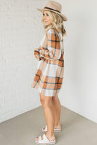 Blonde woman in a fedora wearing a large plaid printed knee length dress with collar, button front, long sleeves with ruffled wrist.