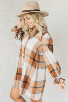 Blonde woman in a fedora wearing a large plaid printed knee length dress with collar, button front, long sleeves with ruffled wrist.