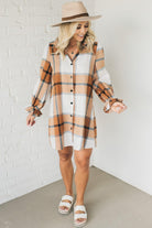 Blonde woman in a fedora wearing a large plaid printed knee length dress with collar, button front, long sleeves with ruffled wrist.