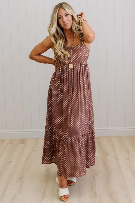 Woman wearing a brown polka dot dress standing against a white paneled wall.