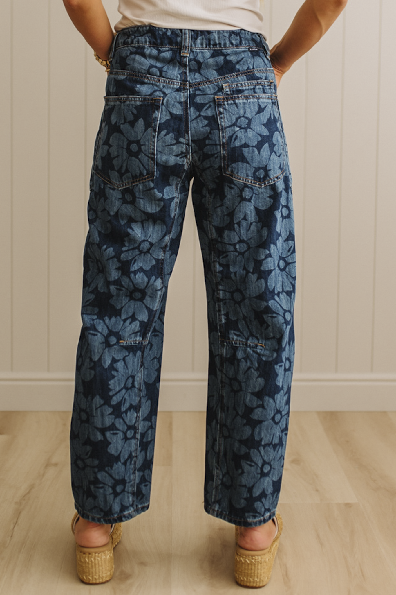 Person wearing blue floral-patterned pants standing against a white paneled wall.