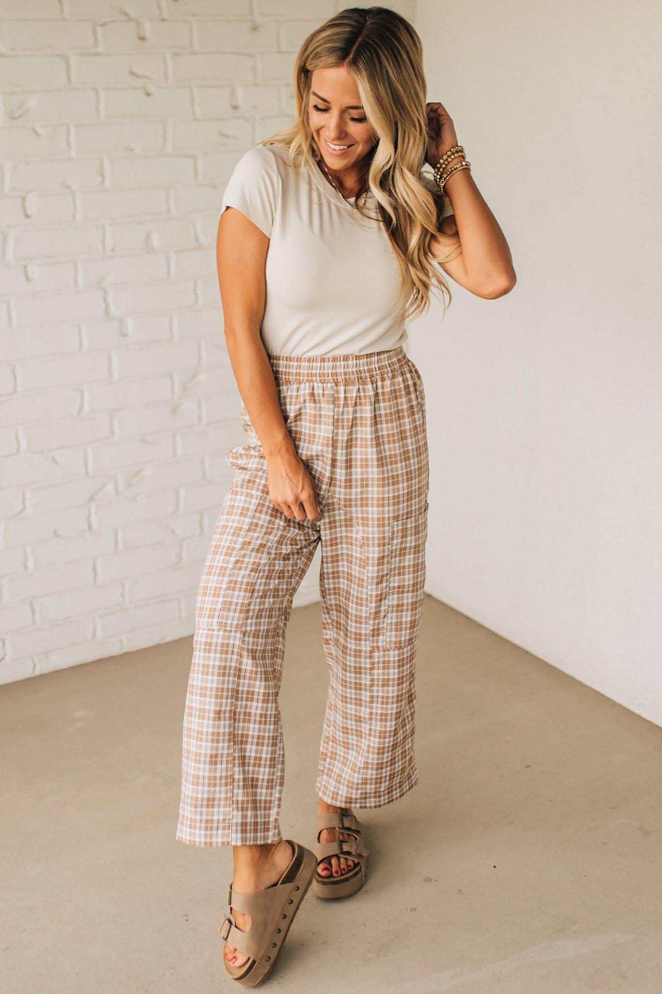 WOMAN WEARING A WHITE TEE AND BROWN SANDALS WITH CHECK PLAID WIDE LEG PANTS WITH THAT HAVE BIG PATCH POCKETS AND ELASTICIZED WAIST.