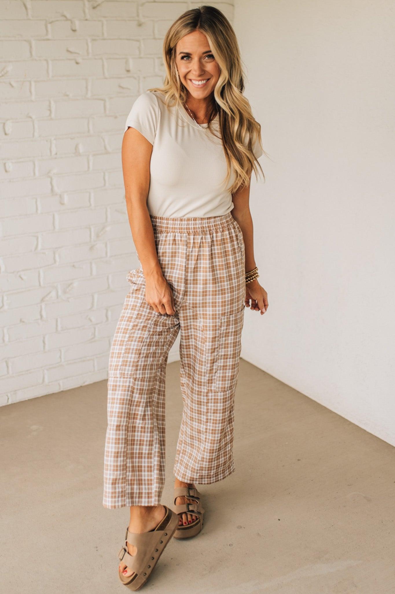 WOMAN WEARING A WHITE TEE AND BROWN SANDALS WITH CHECK PLAID WIDE LEG PANTS WITH THAT HAVE BIG PATCH POCKETS AND ELASTICIZED WAIST.
