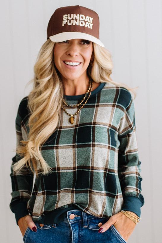 BLONDE WOMAN IN A BROWN HAT WEARING A GREEN CREW NECK, LONG SLEEVE, PLAID PRINTED HACCI TOP