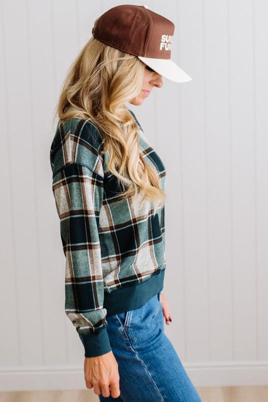 BLONDE WOMAN IN A BROWN HAT WEARING A GREEN CREW NECK, LONG SLEEVE, PLAID PRINTED HACCI TOP
