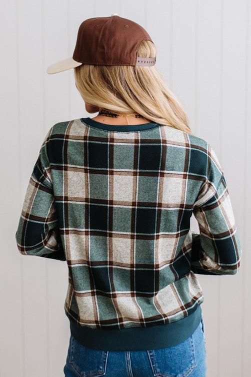 BLONDE WOMAN IN A BROWN HAT WEARING A GREEN CREW NECK, LONG SLEEVE, PLAID PRINTED HACCI TOP