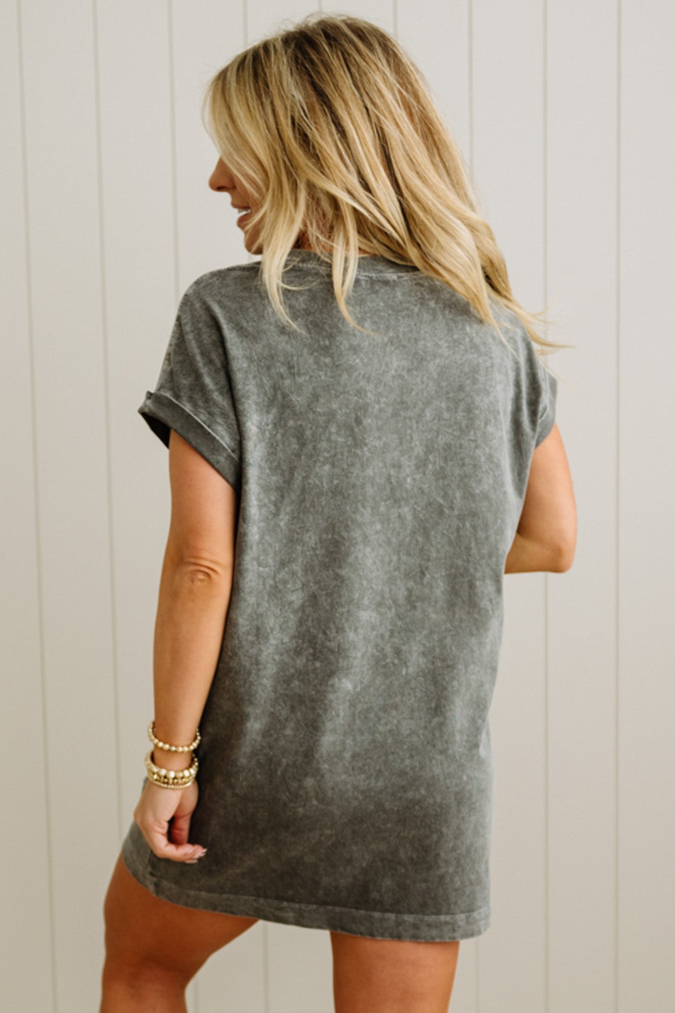 Woman wearing a gray t-shirt dress against a white wooden panel background