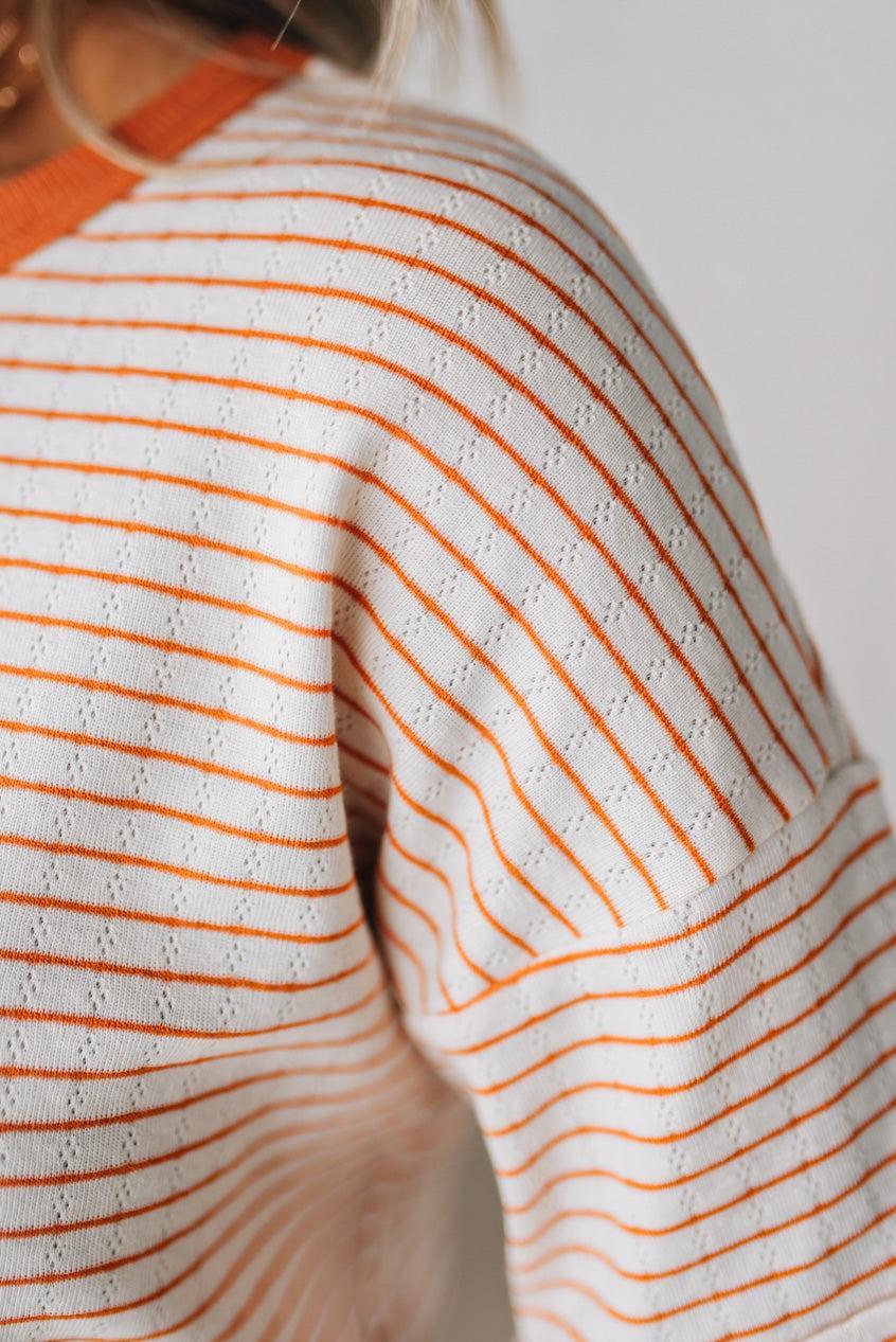 BLONDE WOMAN WEARING A COLOR TRIMMED ROUND NECK, ROLL UP SHORT SLEEVE, POINTELLE STRIPE TOP.