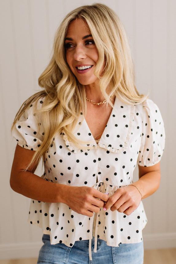 Blonde woman wearing a ivory and black Polka Dot Woven Peter Pan Collar Top with double tie front.