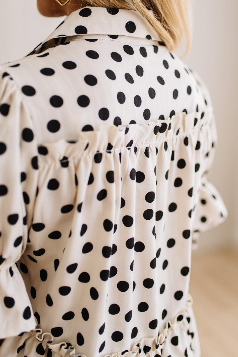 Close-up back view of a woman wearing a cream-colored blouse with black polka dots and ruffled detailing.