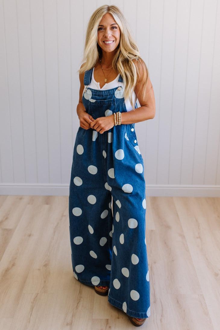 Woman wearing a blue denim jumpsuit with white polka dots against a white wall.