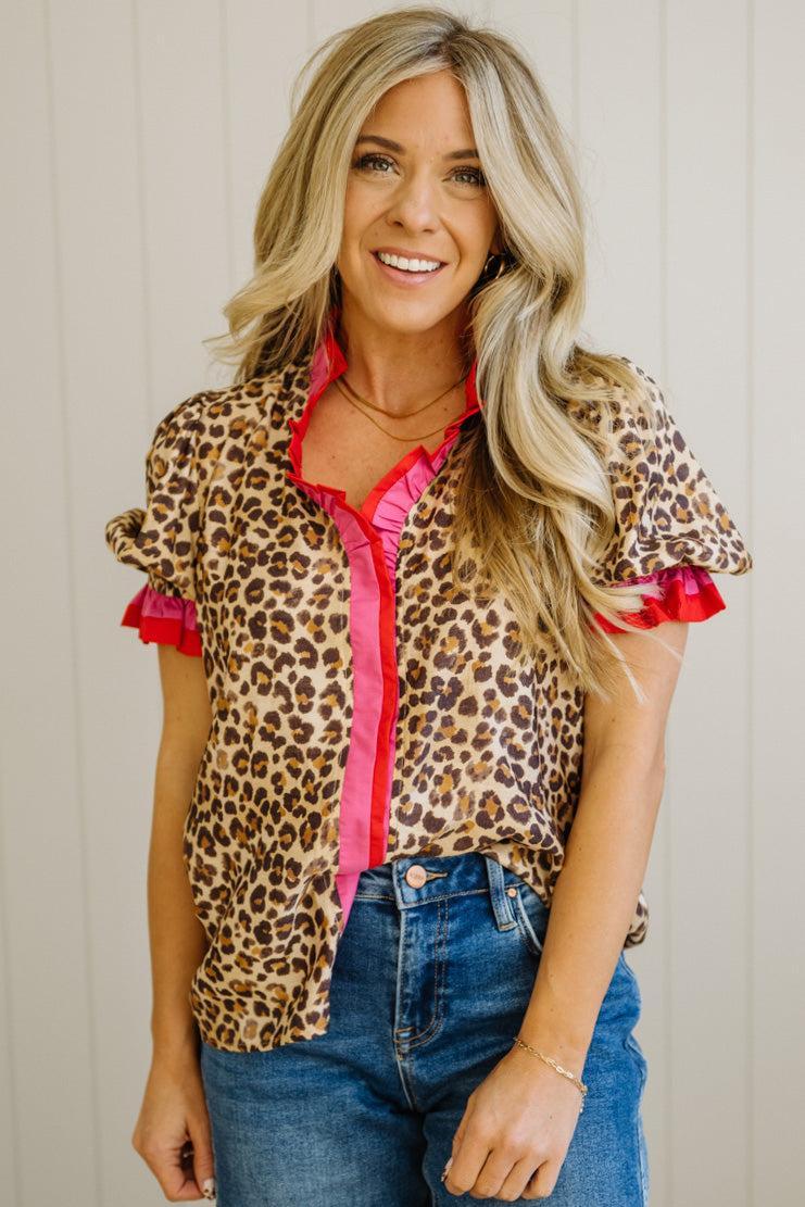 Woman wearing a leopard print blouse with red trim and blue jeans against a neutral background