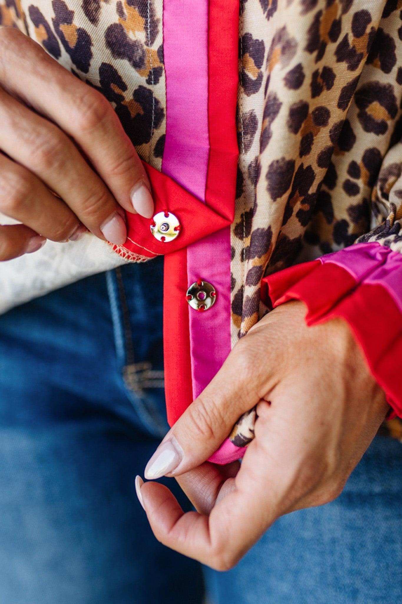 Person adjusting a button on a red garment with a leopard print jacket.