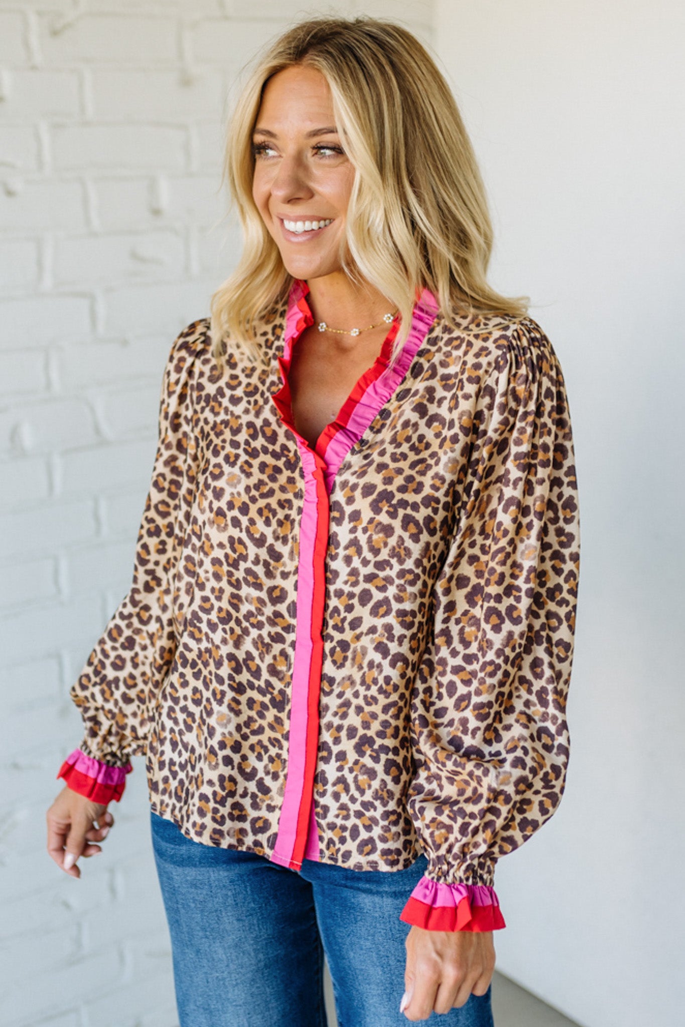 Woman wearing a leopard print shirt with pink accents against a white brick wall.