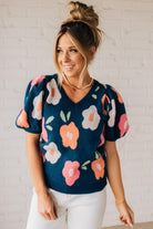 BLONDE WOMAN WEARING A FLORAL PATTERN PUFF SLEEVE SWEATER WITH V-NECK.