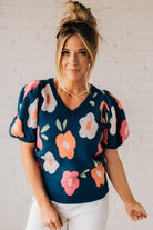 BLONDE WOMAN WEARING A FLORAL PATTERN PUFF SLEEVE SWEATER WITH V-NECK.