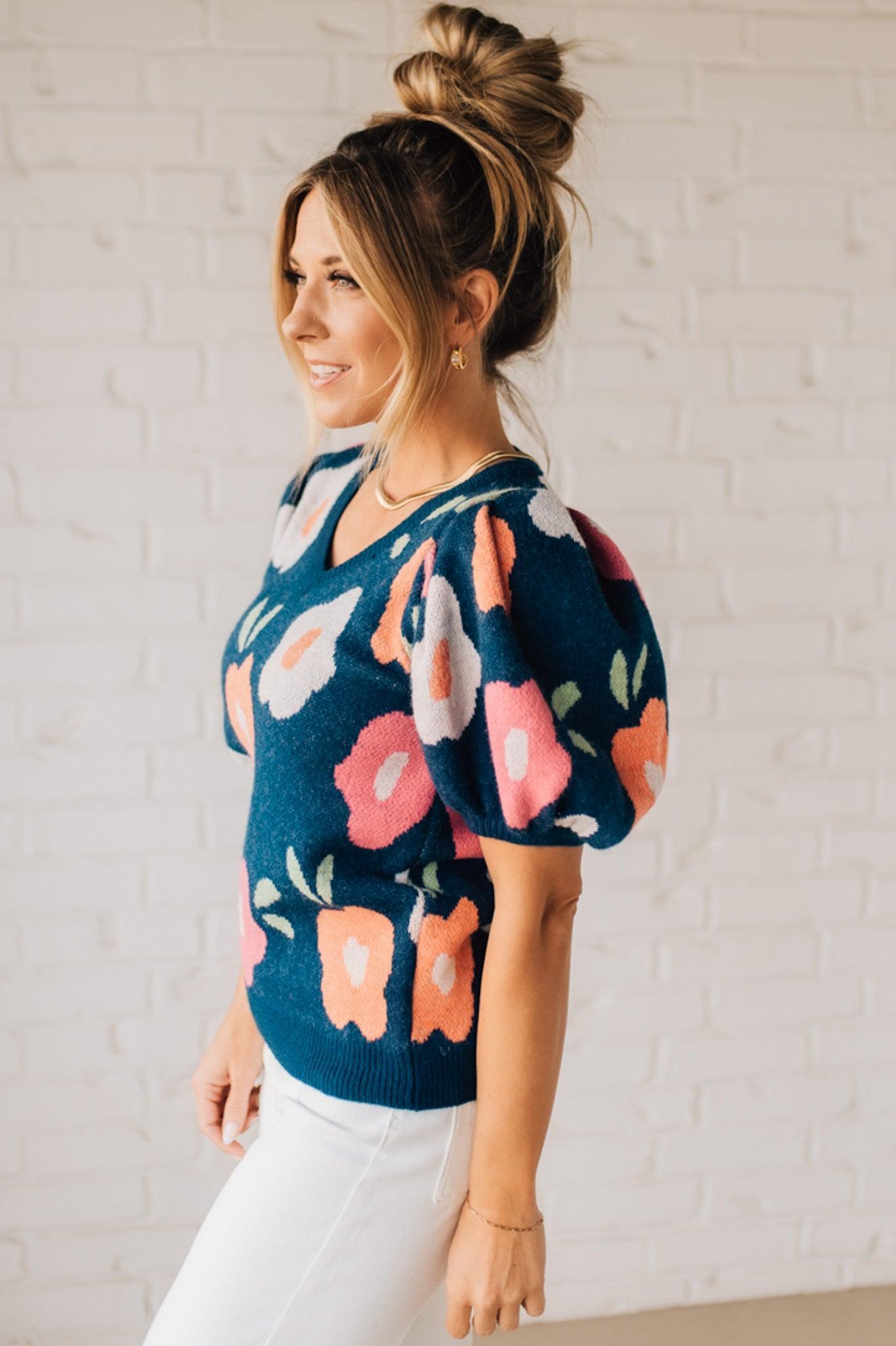 BLONDE WOMAN WEARING A FLORAL PATTERN PUFF SLEEVE SWEATER WITH V-NECK.
