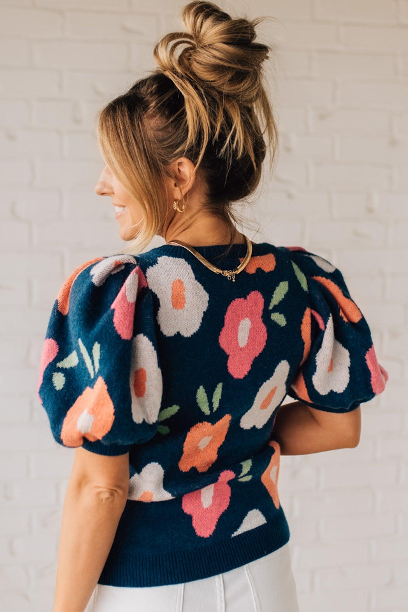 BLONDE WOMAN WEARING A FLORAL PATTERN PUFF SLEEVE SWEATER WITH V-NECK.