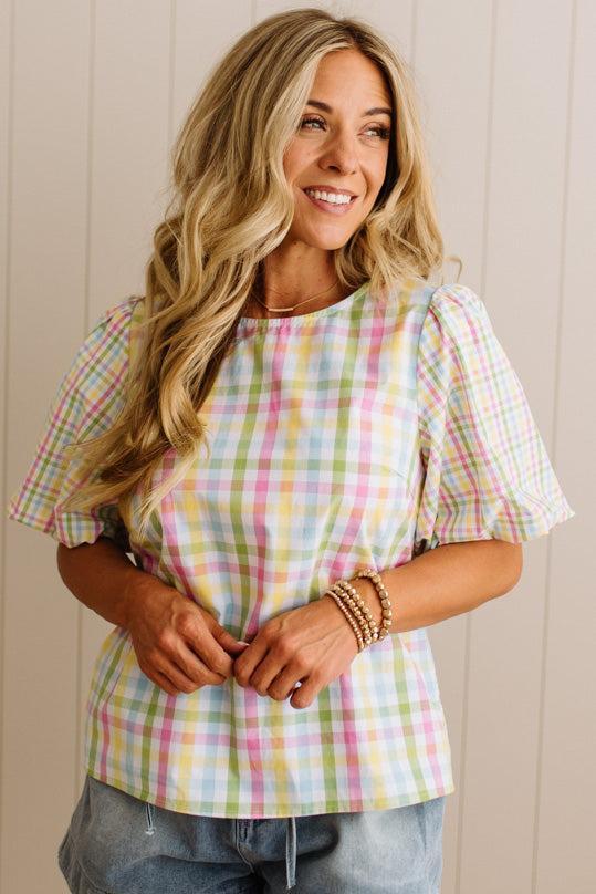 Woman wearing a pastel plaid shirt against a beige wall