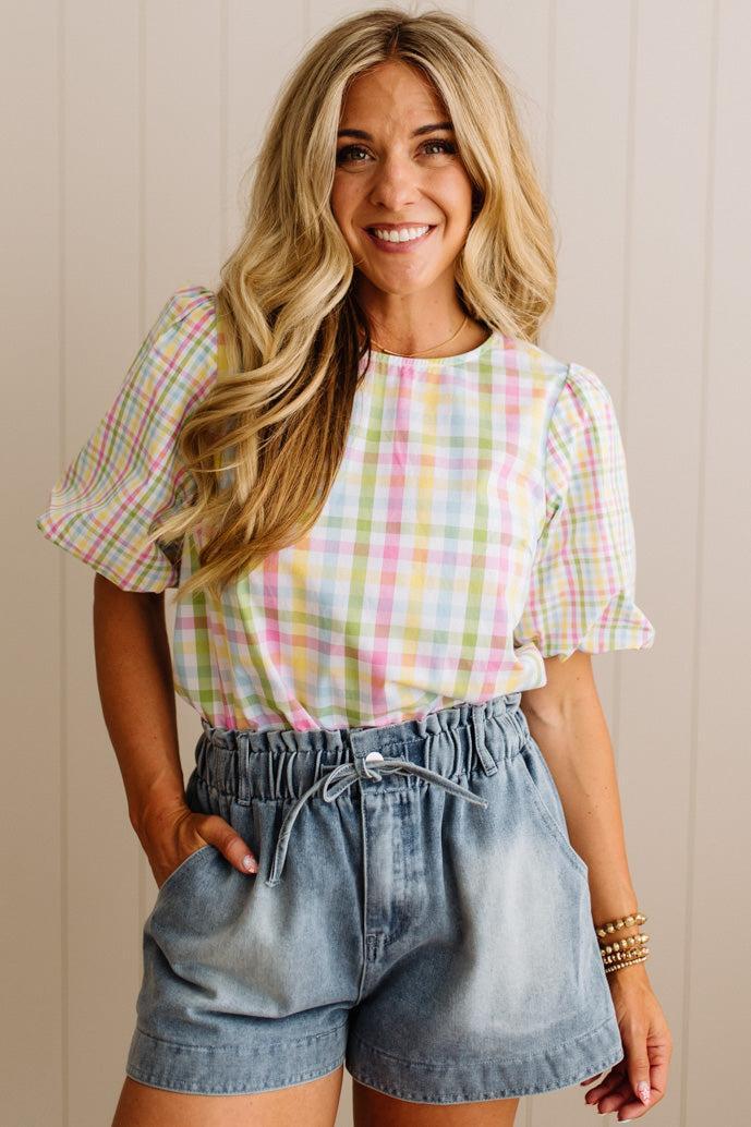 Woman wearing a plaid shirt and denim shorts against a beige wall.