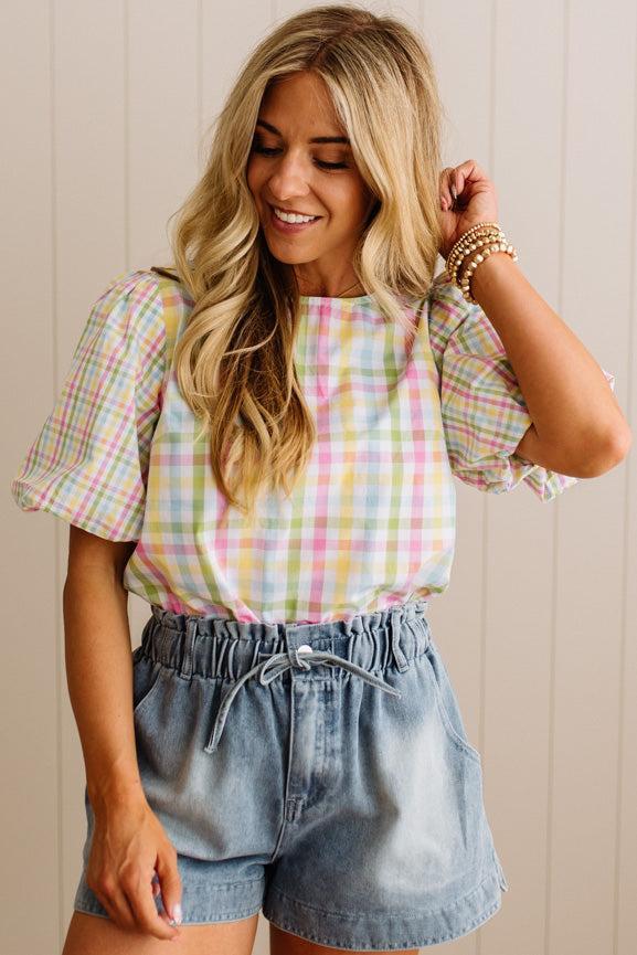 Woman wearing a plaid shirt and denim shorts against a light wooden panel background