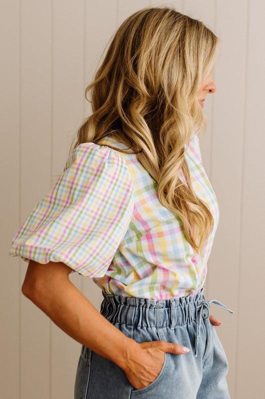 Woman wearing a colorful plaid shirt and light blue jeans against a beige wall.