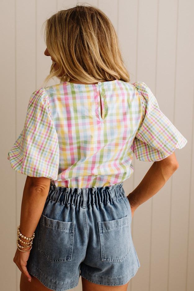 Person wearing a colorful plaid top and denim shorts against a neutral background
