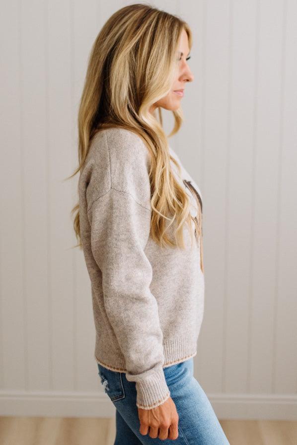 BLONDE WOMAN IN DARK JEANS WEARING A HORSE JACQUARD, STITCH TRIM ACCENT, LONG SLEEVE, CREW NECK PULLOVER SWEATER WITH A HORSE ON THE FRONT, AND WEARING A BIG BELT BUCKLE TOO.
