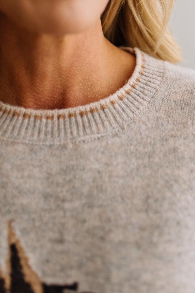 BLONDE WOMAN IN DARK JEANS WEARING A HORSE JACQUARD, STITCH TRIM ACCENT, LONG SLEEVE, CREW NECK PULLOVER SWEATER WITH A HORSE ON THE FRONT, AND WEARING A BIG BELT BUCKLE TOO.