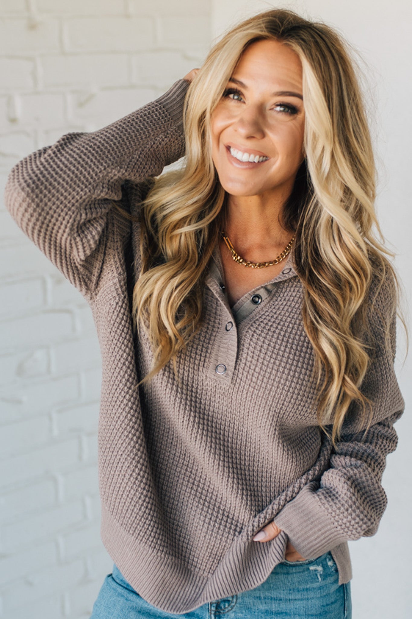 Woman wearing a brown textured sweater against a white brick wall